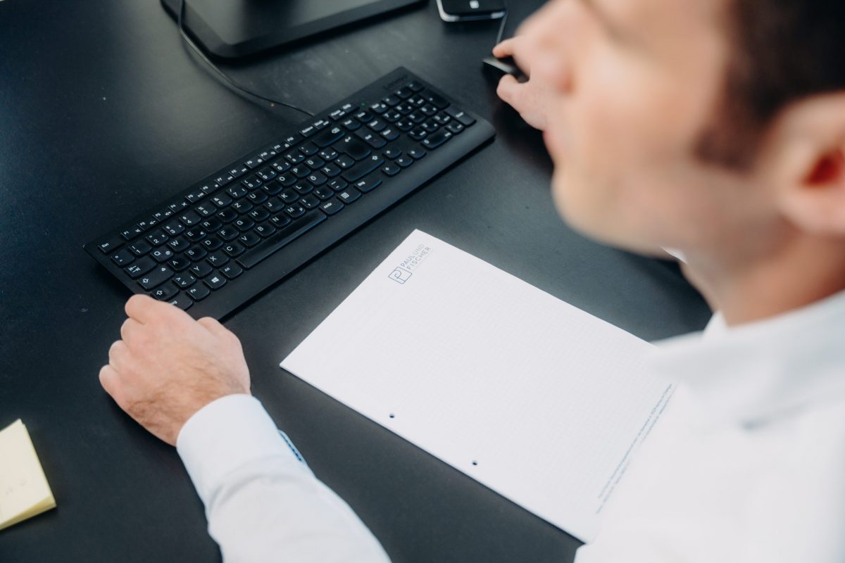 Mann-an-seinem-schwarzen-Schreibtisch Mann mit weißem Hemd an seinem schwarzen Schreibtisch, wo liegen Notizblock und Computertastatur